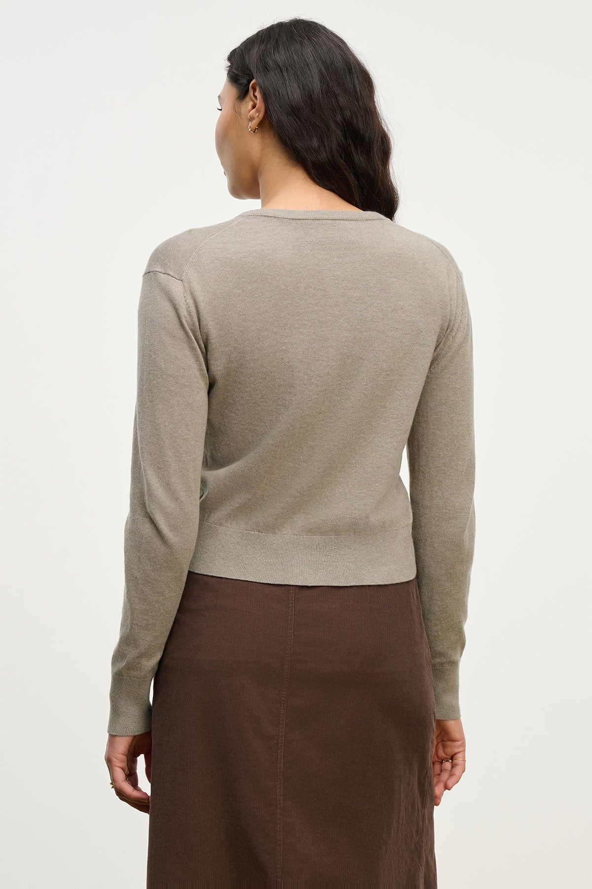 A woman with long dark hair is shown from the back against a plain background, wearing the VIOLETTE CARDIGAN by Velvet by Graham & Spencer in light brown and a dark brown skirt.-39654893453505