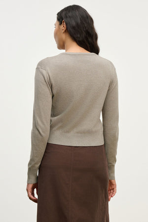 A woman with long dark hair is shown from the back against a plain background, wearing the VIOLETTE CARDIGAN by Velvet by Graham & Spencer in light brown and a dark brown skirt.