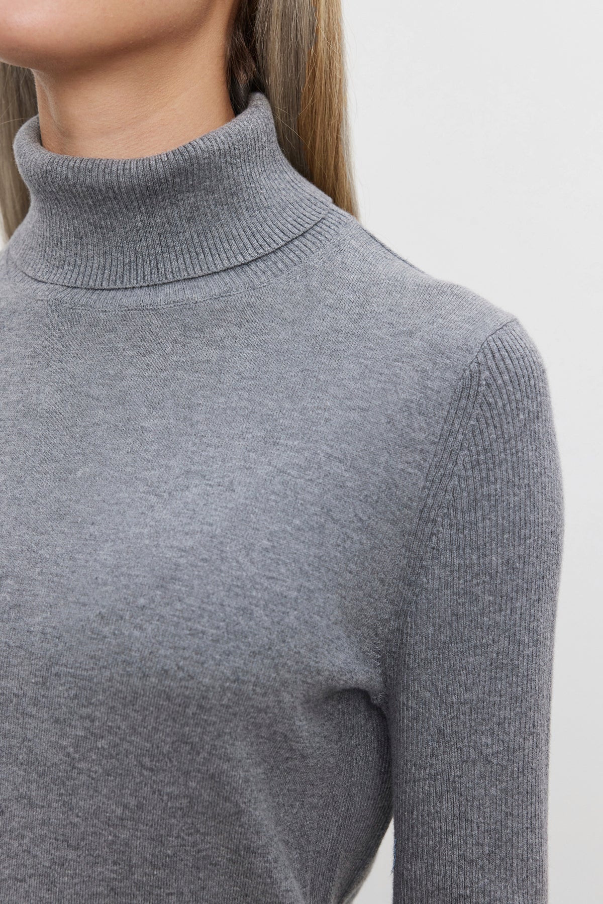   A close-up of a person wearing Velvet by Graham & Spencer's KORIE TURTLENECK SWEATER, featuring ribbed details and long sleeves in a luxurious grey cotton-cashmere blend, viewed from the side. 