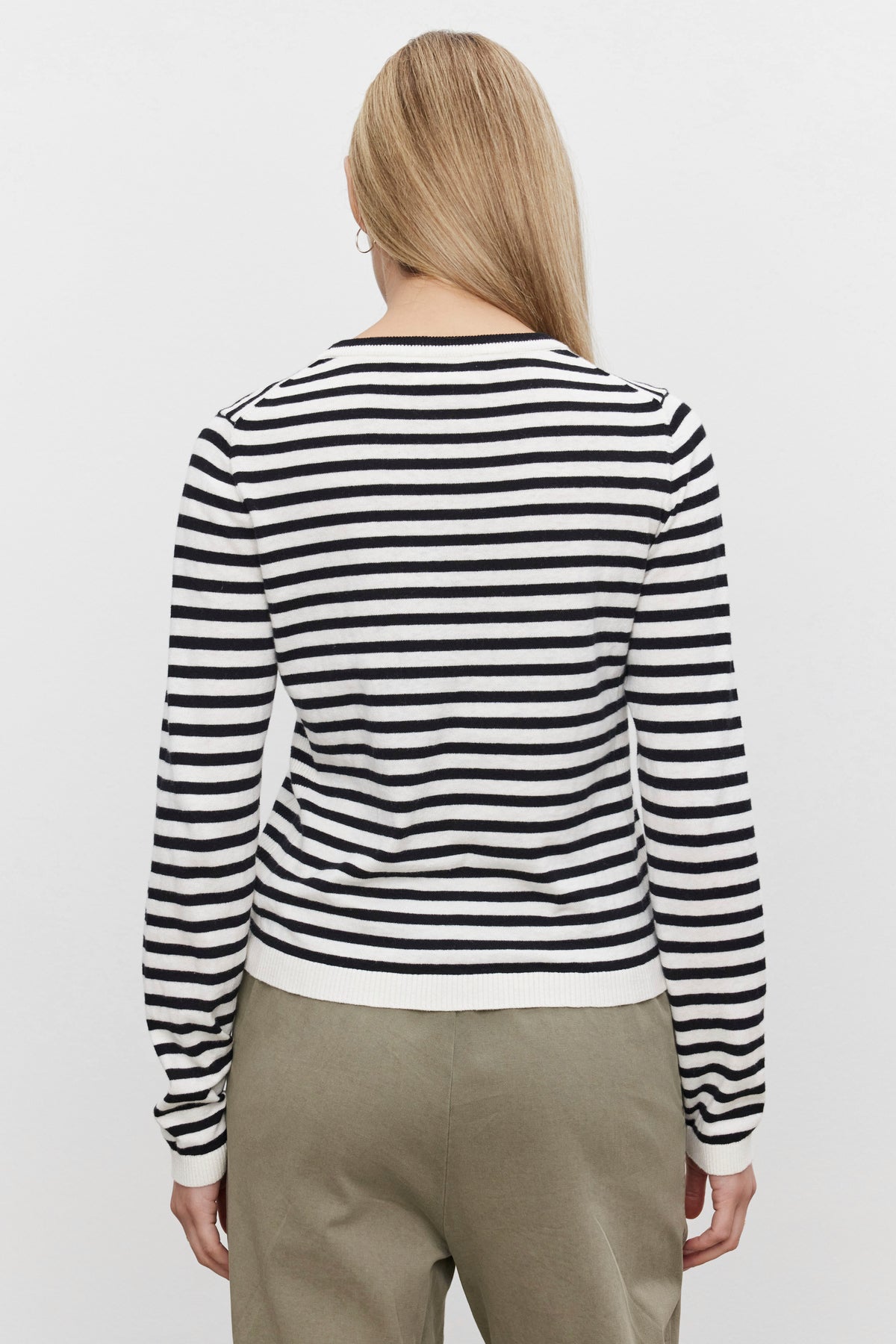   A person with long blonde hair wearing a black and white Velvet by Graham & Spencer ROXY SWEATER made from lux cotton cashmere and beige pants is seen from the back against a plain white background. 