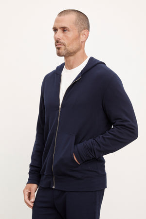 A man in a navy blue non-bulky fit RODAN LUXE FLEECE ZIP HOODIE and matching pants, standing with his hand on his hip, looking to his left by Velvet by Graham & Spencer.