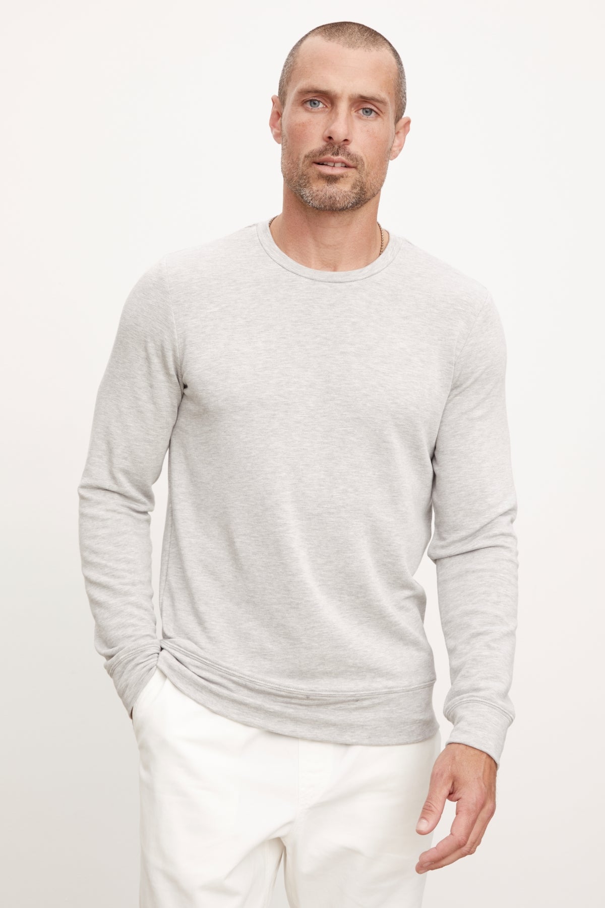   A man wearing the SOREN PULLOVER from Velvet by Graham & Spencer and white pants stands against a plain backdrop, highlighting the cozy brushed interior that makes it perfect workout gear. 