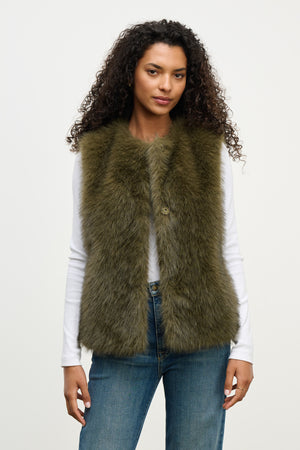 A woman models the ANASTASIA FAUX FUR VEST by Velvet by Graham & Spencer over a white long-sleeve shirt and blue jeans—a chic, plush layering piece for cold-weather style.