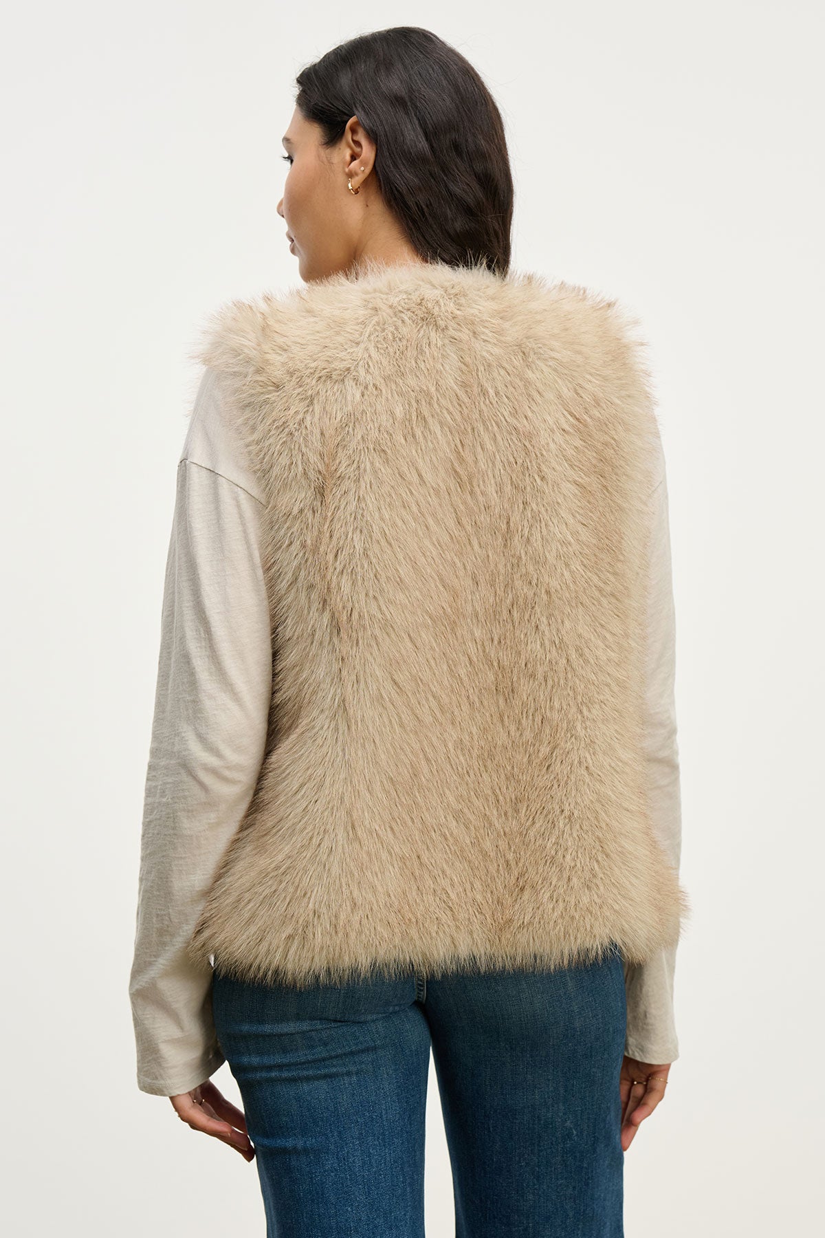 A person wears the ANASTASIA FAUX FUR VEST by Velvet by Graham & Spencer over a long-sleeve shirt and blue jeans, shown from the back against a plain background—a stylish staple for cold-weather wardrobes.-39815139721409