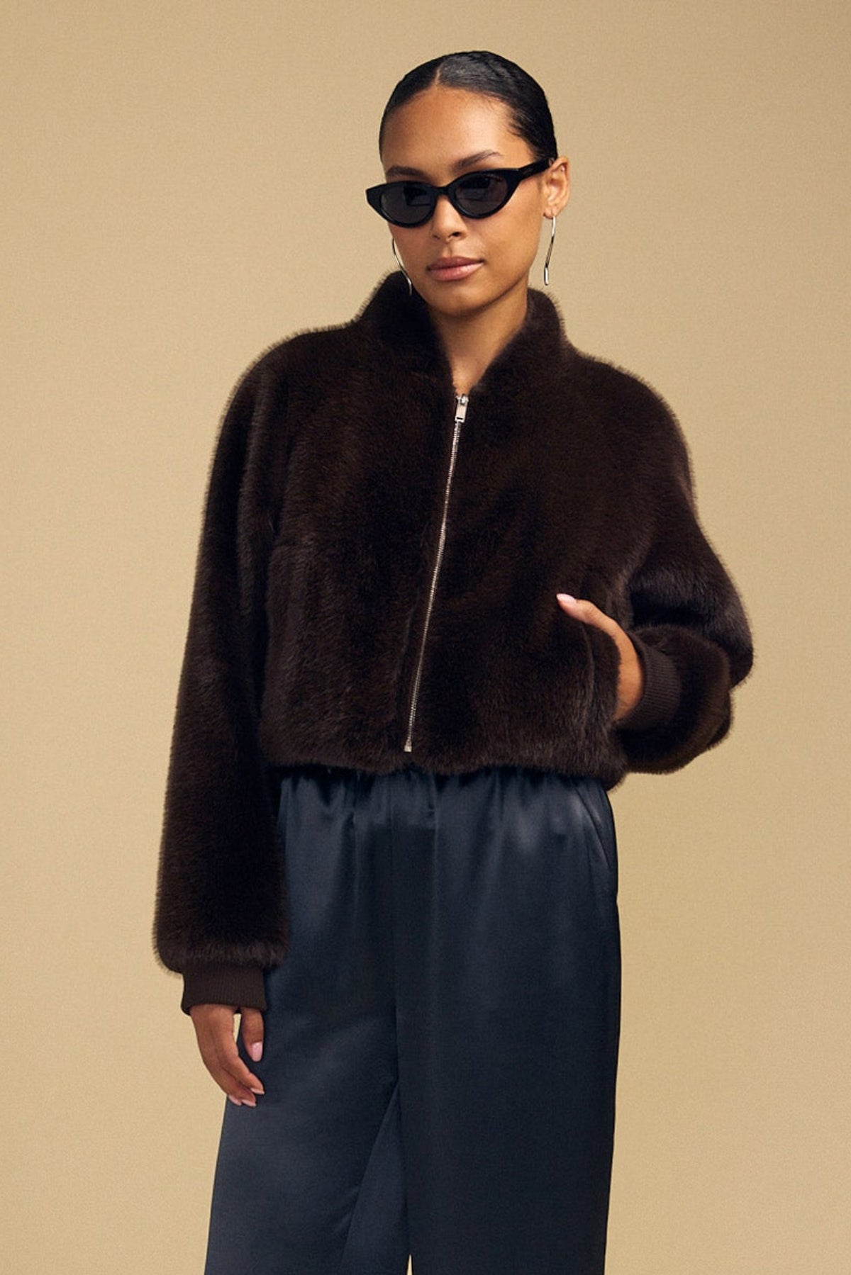 A person wearing a dark brown ARIANNA FAUX FUR BOMBER JACKET by Velvet by Graham & Spencer and black trousers.-46488089919681
