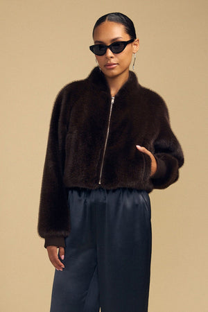 A person wearing a dark brown ARIANNA FAUX FUR BOMBER JACKET by Velvet by Graham & Spencer and black trousers.