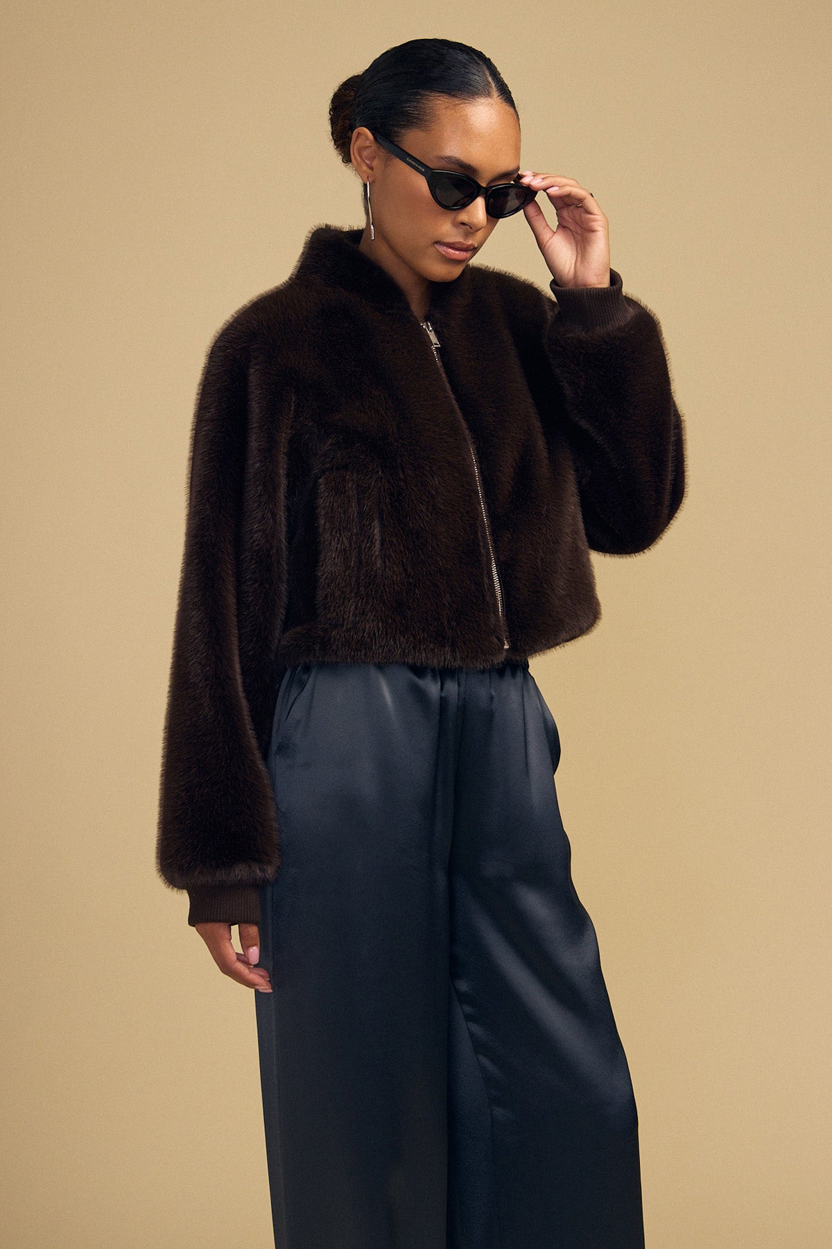 A person wearing a dark brown ARIANNA FAUX FUR BOMBER JACKET by Velvet by Graham & Spencer and dark trousers.