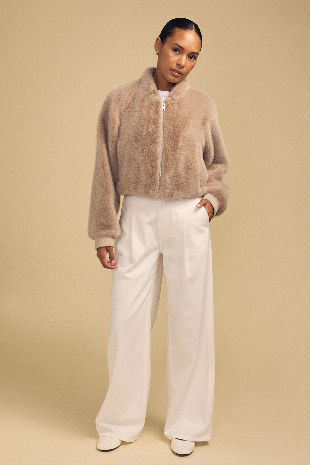 A person wearing an ARIANNA FAUX FUR BOMBER JACKET by Velvet by Graham & Spencer with wide-leg white trousers.-46488090083521