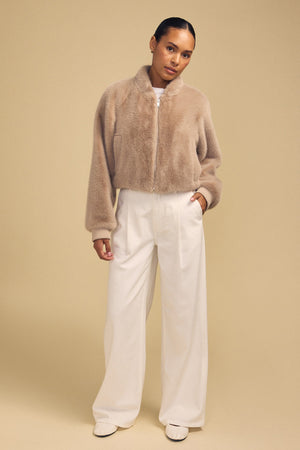 A person wearing an ARIANNA FAUX FUR BOMBER JACKET by Velvet by Graham & Spencer with wide-leg white trousers.