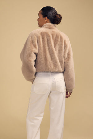A person seen from behind, wearing an ARIANNA FAUX FUR BOMBER JACKET in beige and white trousers.