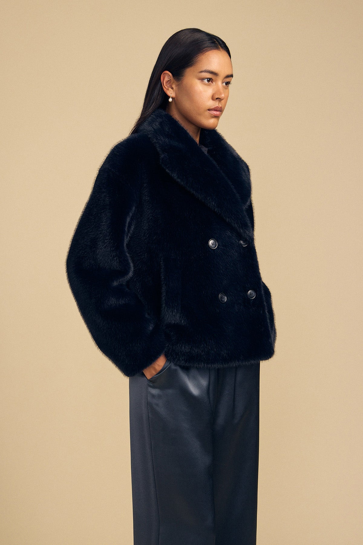 A person wears a black double-breasted CHARLOTTE FAUX FUR JACKET by Velvet by Graham & Spencer, featuring a notched collar as a statement layer.