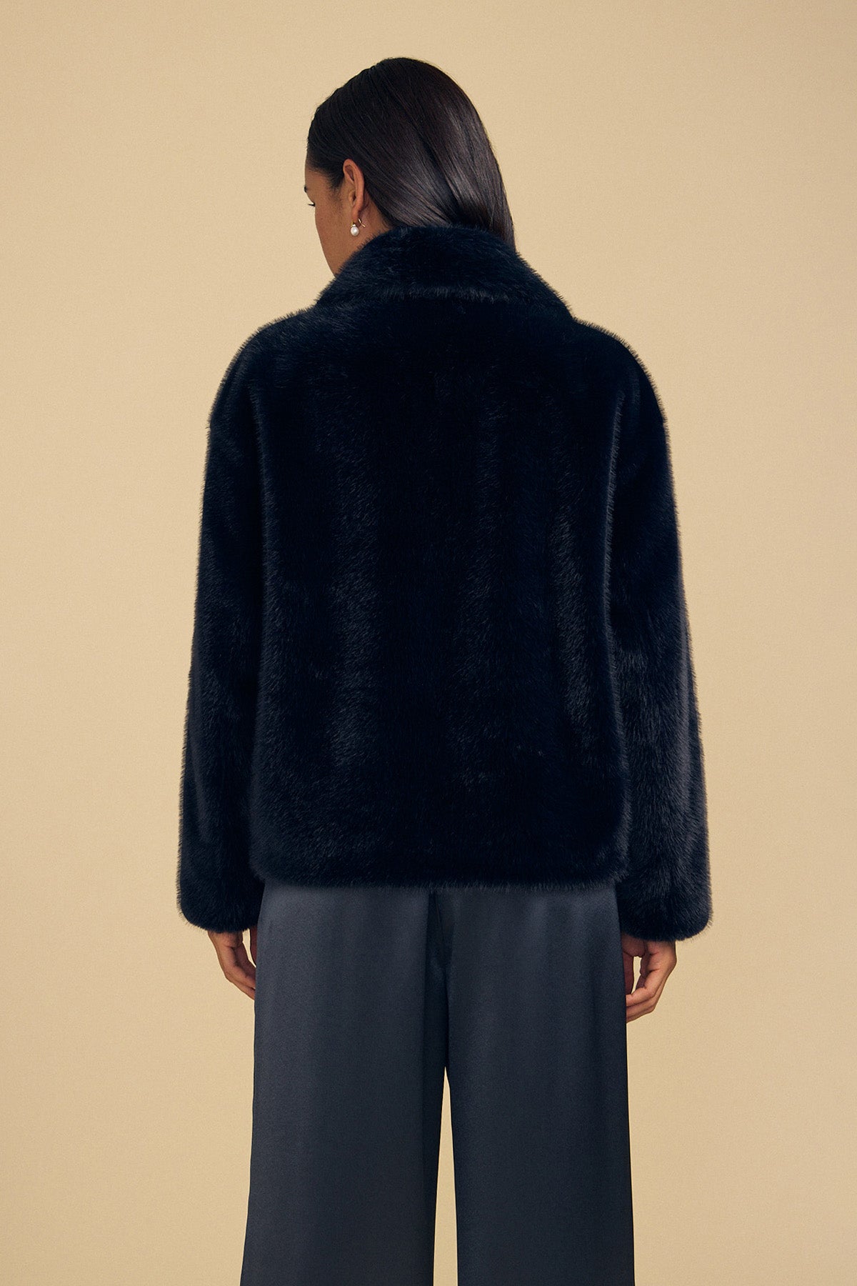 A person seen from behind wearing a black faux fur CHARLOTTE FAUX FUR JACKET and dark trousers.