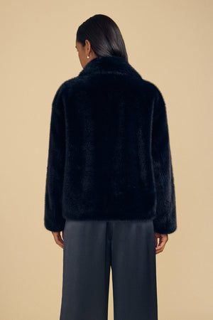 A person seen from behind wearing a black faux fur CHARLOTTE FAUX FUR JACKET and dark trousers.