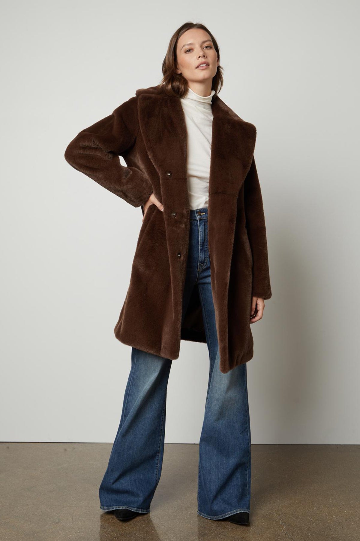   The model is wearing a brown EVALYN LUX FAUX FUR COAT by Velvet by Graham & Spencer. 