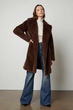 The model is wearing a brown EVALYN LUX FAUX FUR COAT by Velvet by Graham & Spencer.