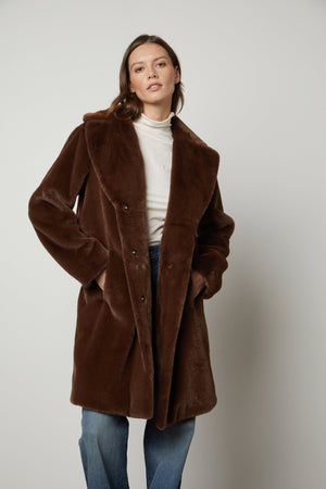 A model wearing a Brown EVALYN LUX FAUX FUR COAT by Velvet by Graham & Spencer strikes a silhouette.