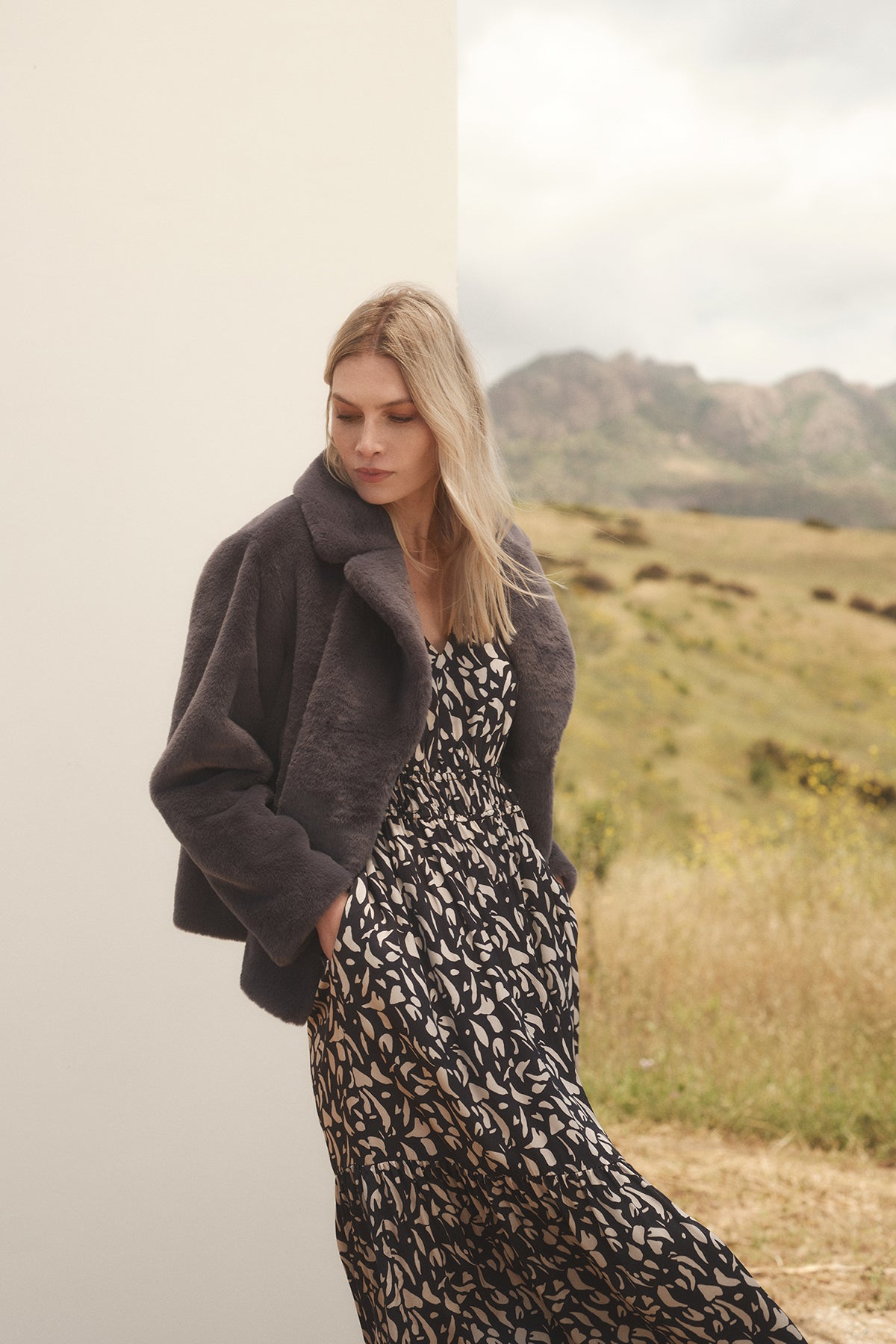   A woman in a LYUDA PRINTED SATIN MIDI DRESS by Velvet by Graham & Spencer with a v-neckline and a grey faux fur jacket. 