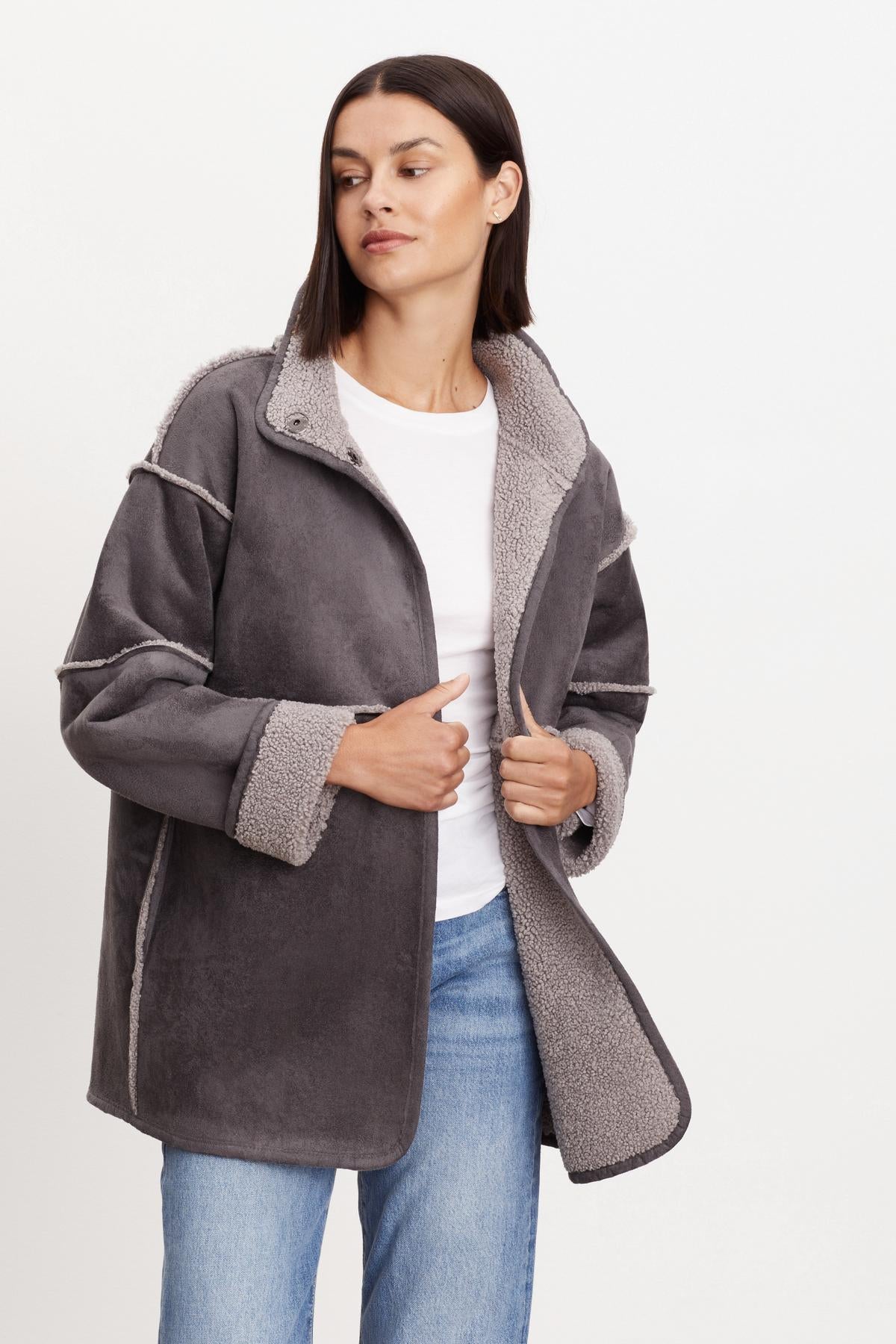 A person wearing a gray ALBANY LUX SHERPA REVERSIBLE JACKET by Velvet by Graham & Spencer over a white shirt and blue jeans stands against a plain background.-36094290919617