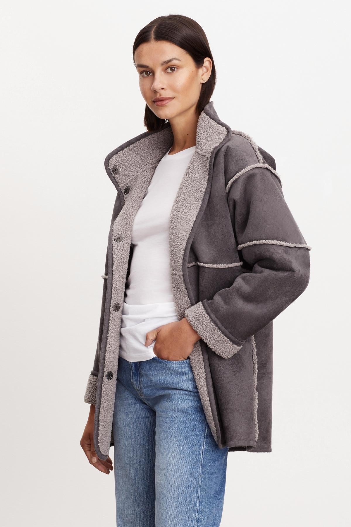 A person stands wearing a Velvet by Graham & Spencer ALBANY LUX SHERPA REVERSIBLE JACKET over a white shirt and blue jeans, with one hand in their pocket. They have dark hair and are looking directly at the camera.-36094291083457