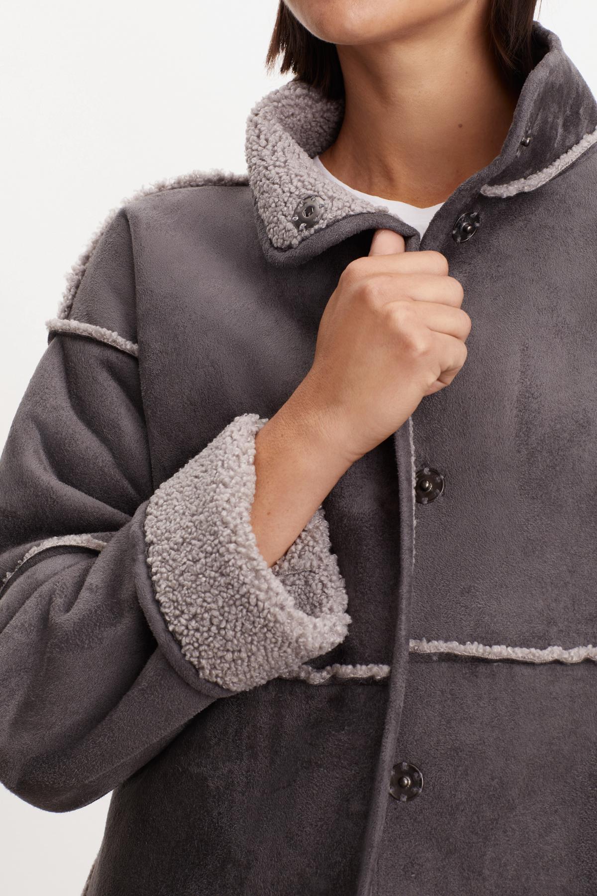   Person wearing a gray Velvet by Graham & Spencer ALBANY LUX SHERPA REVERSIBLE JACKET, holding the collar with one hand. 