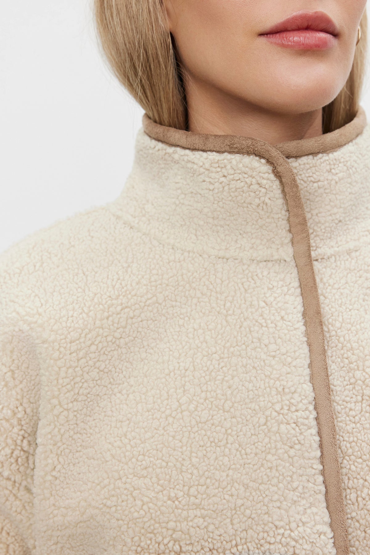 A close-up of a partially visible person wearing the ALBANY LUXE SHERPA REVERSIBLE JACKET by Velvet by Graham & Spencer, featuring an eco-friendly design in cream with brown trim and a high collar.-37676889571521