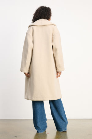 A person stands facing away, wearing the Velvet by Graham & Spencer ELEANOR SHERPA REVERSIBLE COAT and wide-leg blue jeans against a plain white background.