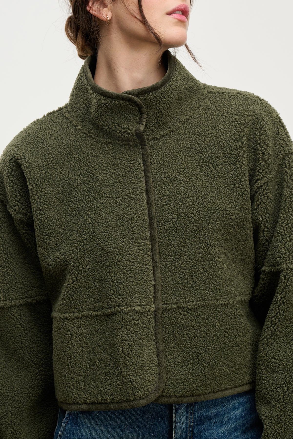 A person wearing the Velvet by Graham & Spencer KELLY LUXE SHERPA REVERSIBLE JACKET in olive green, featuring a high neck and textured faux sherpa fleece, paired with blue jeans and shown from shoulders to waist.-39800351981761