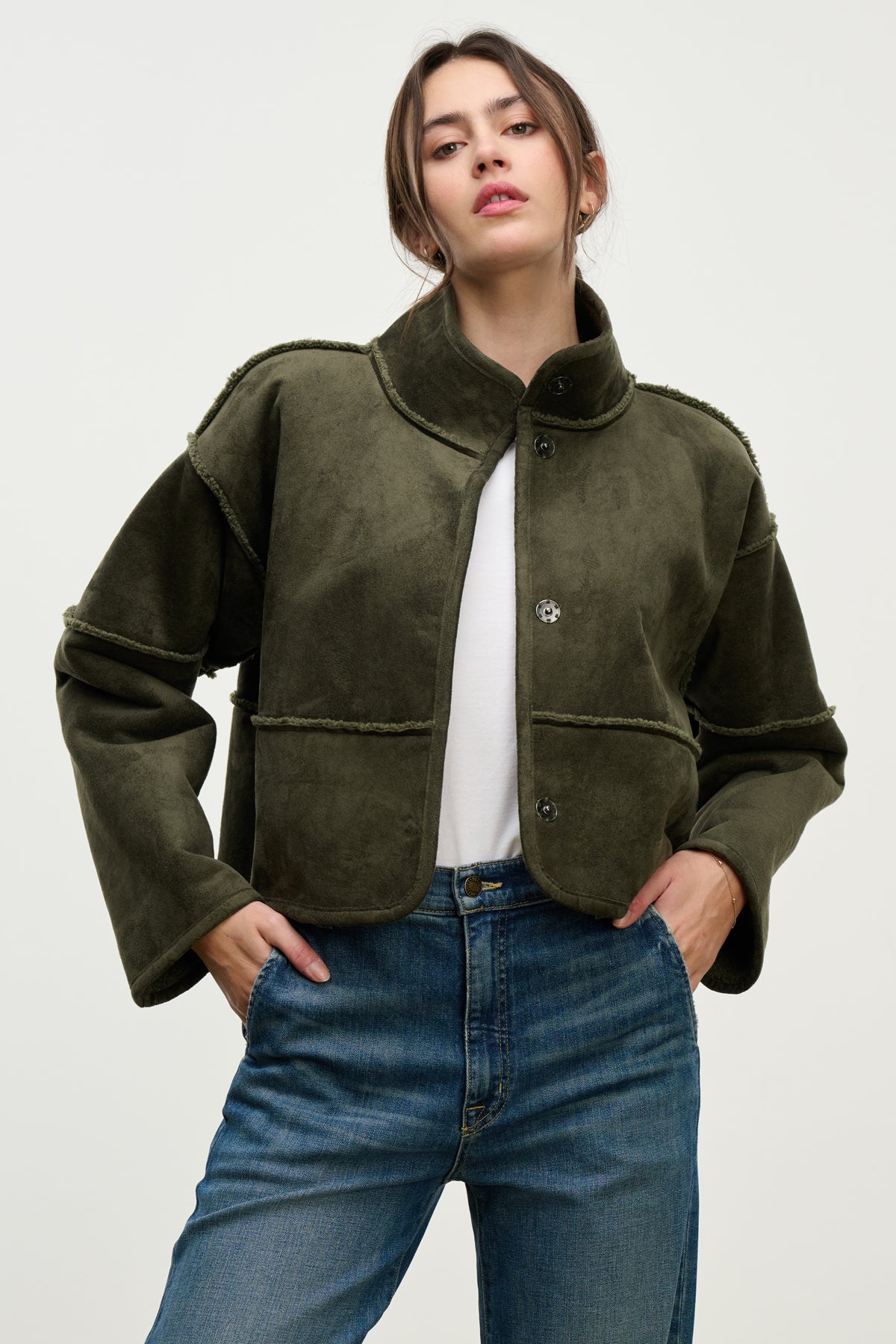  A woman stands against a plain background with her hands in her pockets, wearing the KELLY LUXE SHERPA REVERSIBLE JACKET by Velvet by Graham & Spencer over a white shirt and blue jeans. 