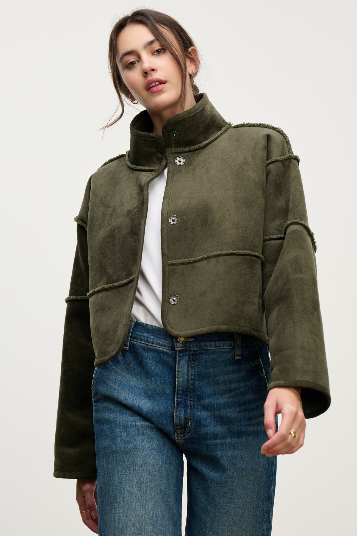   A woman wears the KELLY LUXE SHERPA REVERSIBLE JACKET by Velvet by Graham & Spencer over a white shirt and blue jeans, standing against a plain light background. 