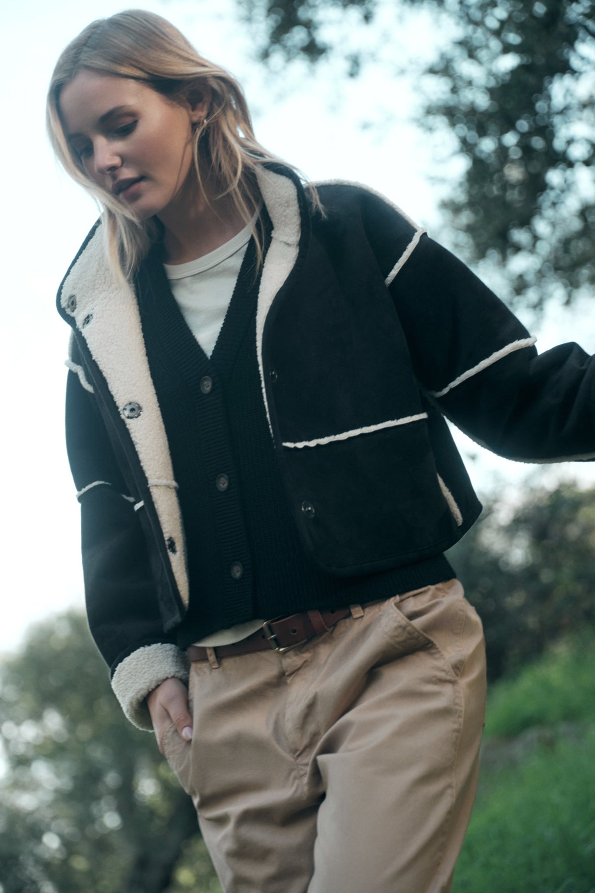   A person in the KELLY LUXE SHERPA REVERSIBLE JACKET by Velvet by Graham & Spencer and beige pants walks outdoors with trees in the background. 