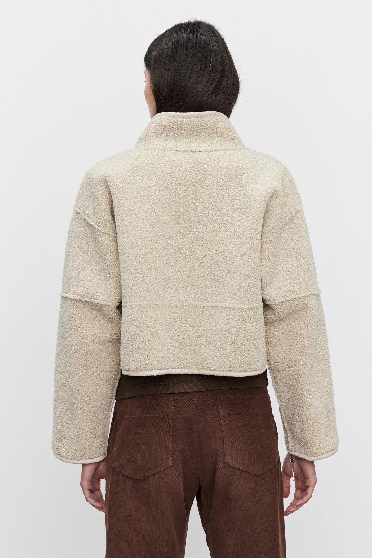   A person is wearing the KELLY LUXE SHERPA REVERSIBLE JACKET by Velvet by Graham & Spencer in beige, along with brown pants, shown from the back against a plain background. 