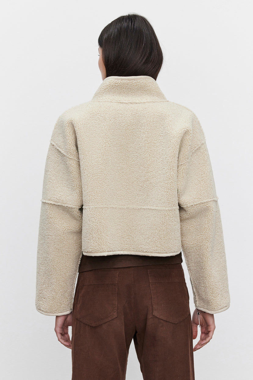 A person is wearing the KELLY LUXE SHERPA REVERSIBLE JACKET by Velvet by Graham & Spencer in beige, along with brown pants, shown from the back against a plain background.