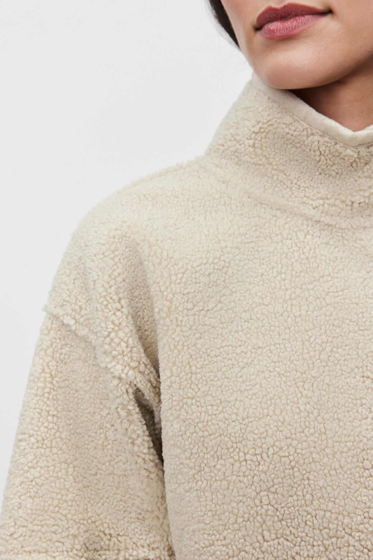   Close-up of a person wearing the beige, textured KELLY LUXE SHERPA REVERSIBLE JACKET by Velvet by Graham & Spencer, highlighting the collar and shoulder area against a plain background. 