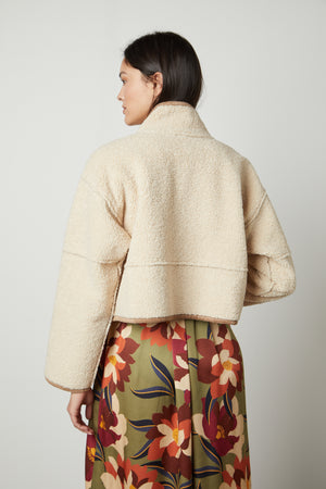 The back view of a person wearing a Velvet by Graham & Spencer KELLY LUX SHERPA REVERSIBLE JACKET and floral skirt.