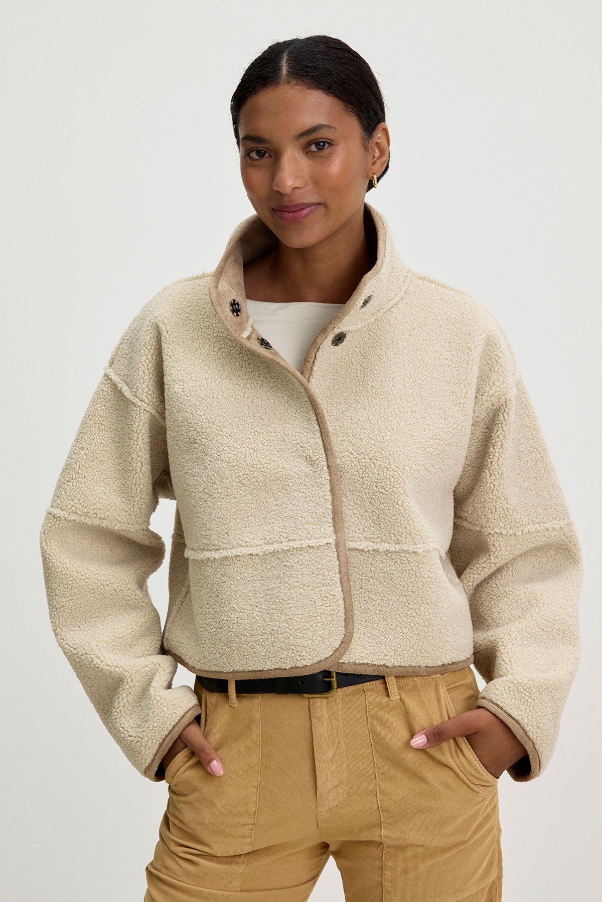 A person in a KELLY LUXE SHERPA REVERSIBLE JACKET from Velvet by Graham & Spencer and tan pants stands against a plain background, hands in pockets.-37856005882049