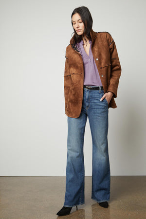 The model is wearing a cozy brown suede jacket, the LAILA PRINTED SHERPA REVERSIBLE JACKET by Velvet by Graham & Spencer.