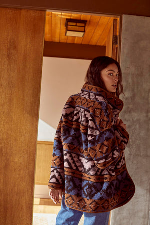 A woman is standing in a doorway wearing a Velvet by Graham & Spencer LAILA PRINTED SHERPA REVERSIBLE JACKET.