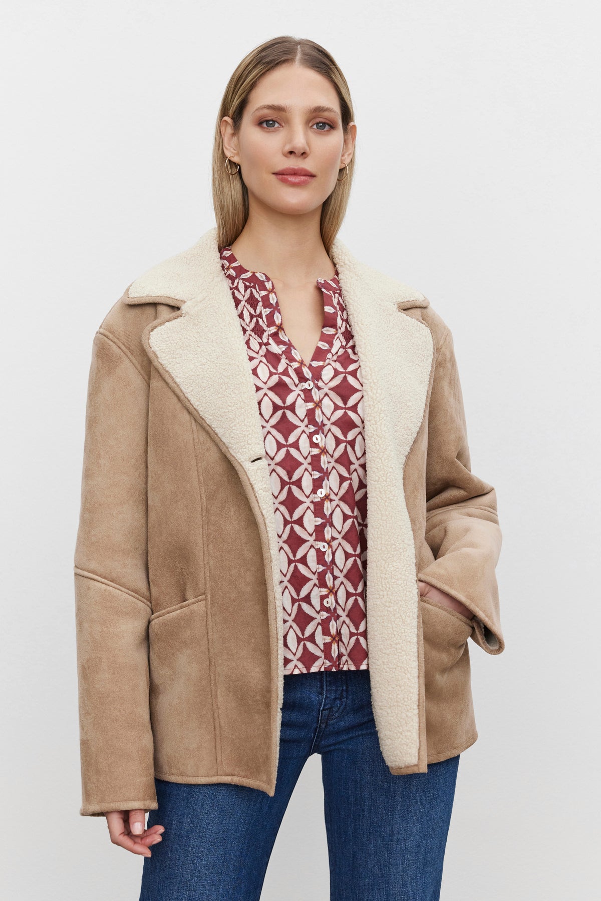   A person wearing the MOLLY LUXE SHERPA JACKET from Velvet by Graham & Spencer over a red patterned blouse and blue jeans stands against a plain white background. 