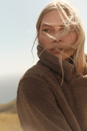 An eco-friendly woman in a YOKO LUX SHERPA OVERSIZED JACKET by Velvet by Graham & Spencer is standing on a winter hill.