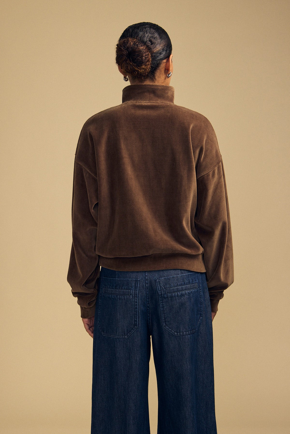 Back view of a person wearing a brown DANICA VELOUR HALF-ZIP SWEATSHIRT and dark blue jeans.-46488235802817