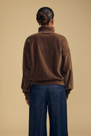 Back view of a person wearing a brown DANICA VELOUR HALF-ZIP SWEATSHIRT and dark blue jeans.