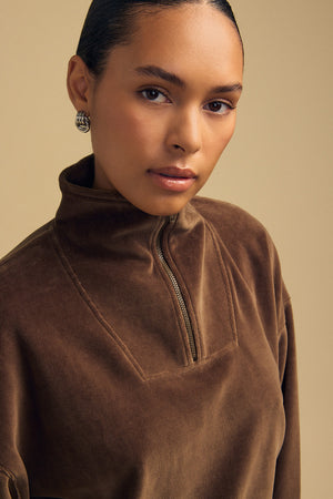 Close-up of a person wearing a brown DANICA VELOUR HALF-ZIP SWEATSHIRT with a mock neck.