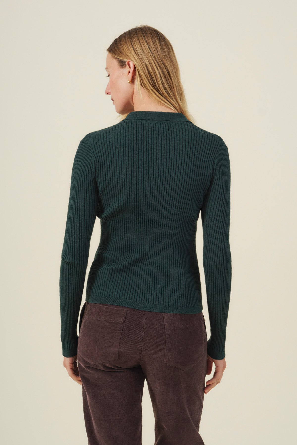 A person with long blonde hair, seen from behind against a light background, wears the Velvet by Graham & Spencer FRANCES SWEATER POLO in dark green ribbed cotton-cashmere, paired with dark brown pants.-41834330783937