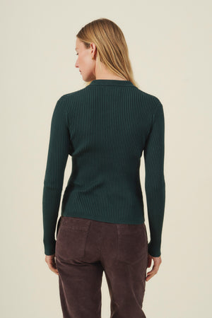 A person with long blonde hair, seen from behind against a light background, wears the Velvet by Graham & Spencer FRANCES SWEATER POLO in dark green ribbed cotton-cashmere, paired with dark brown pants.