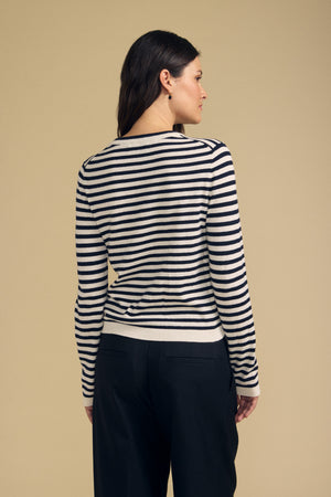 A person stands facing away against a beige background, wearing the ROXY SWEATER by Velvet by Graham & Spencer— a black and white striped sweater— paired with black pants.