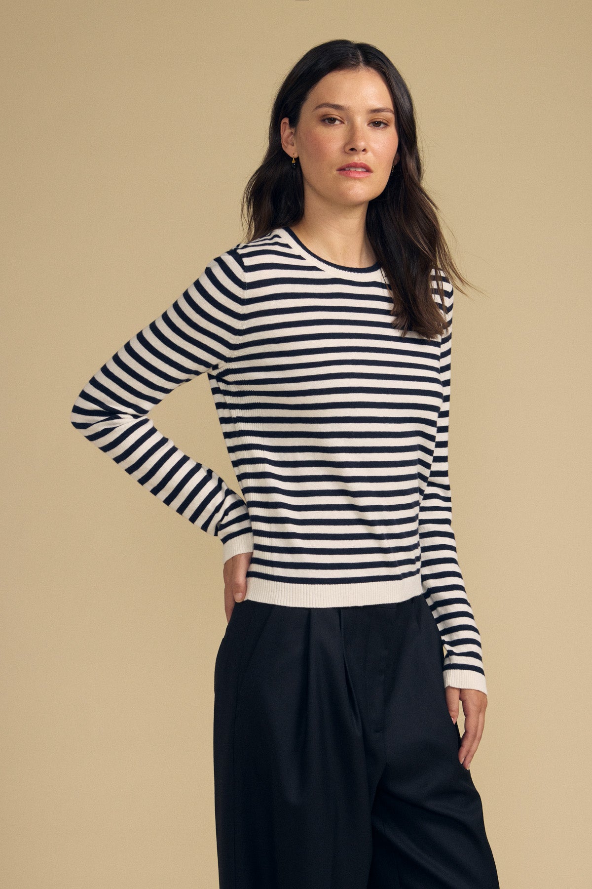 A model wears the ROXY SWEATER by Velvet by Graham & Spencer, featuring black-and-white stripes, paired with black pants against a plain beige background.-41965253853377