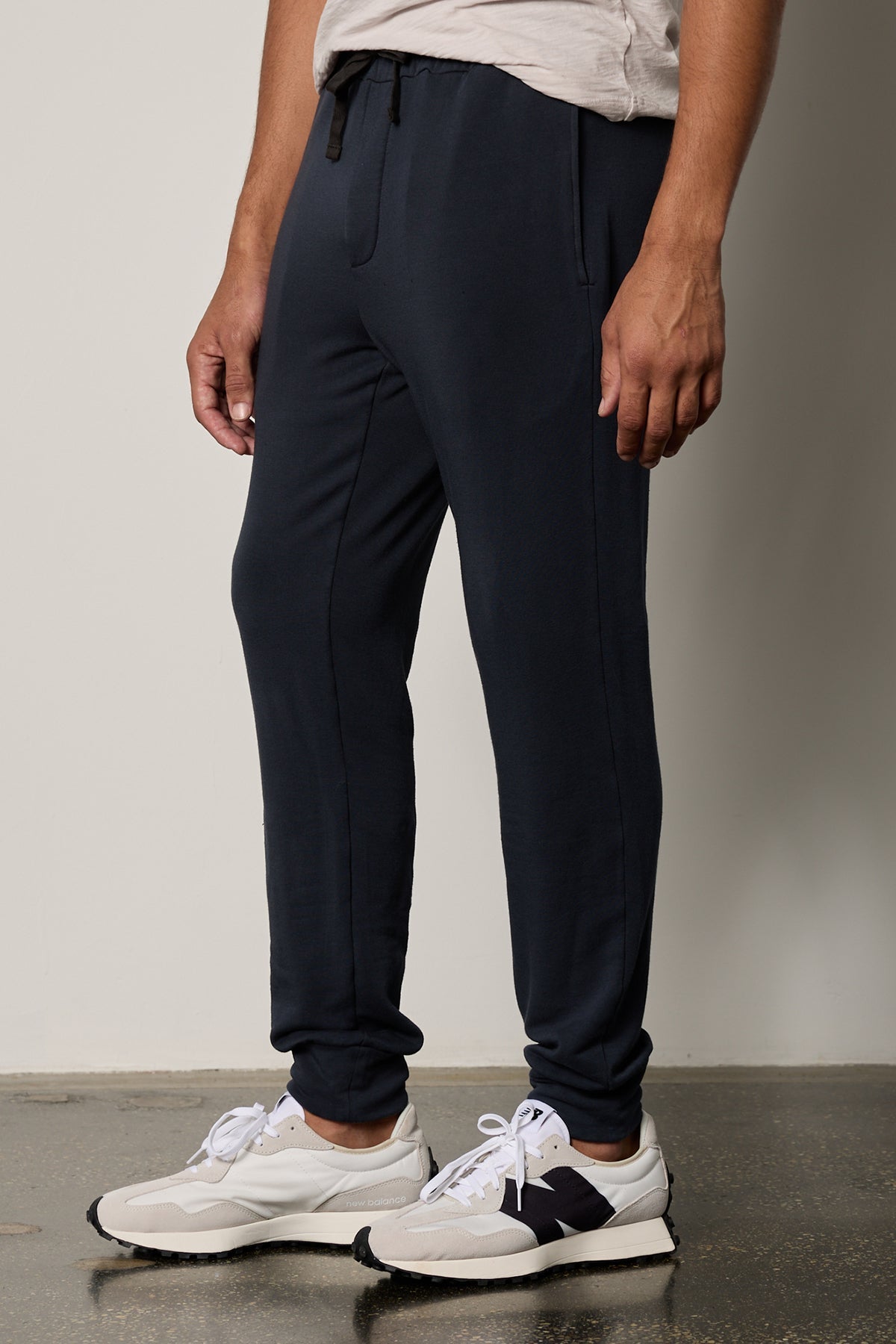   A man wearing Velvet by Graham & Spencer's CROSBY LUXE FLEECE JOGGER sweatpants and white sneakers, showcasing a tailored design and go-anywhere essential style. 