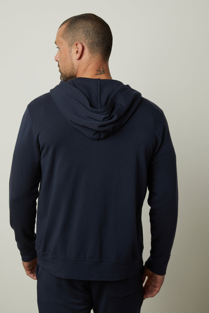 A man wearing a navy blue RODAN HOODIE with the hood down, made from luxe fleece by Velvet by Graham & Spencer, stands with his back to the camera.