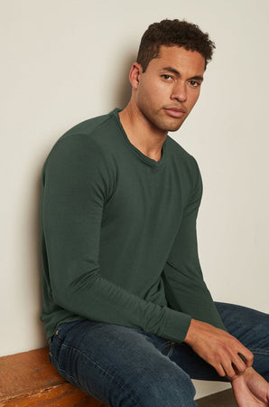 A man wearing a cozy green long-sleeved SOREN LUXE FLEECE PULLOVER made by Velvet by Graham & Spencer and stretch jeans.