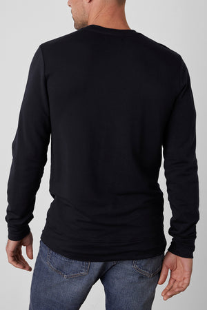 A man wearing a SOREN PULLOVER in cozy black from Velvet by Graham & Spencer and blue jeans, seen from the back.